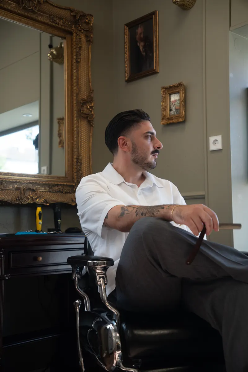 Friseurmeister Christopher Keanu Reinhardt sitzt mit Rasiermesser in der Hand im Salon