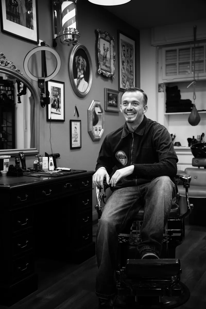 Faik, Barbier, sitzt im Barber-Stuhl vor der Bilderwand